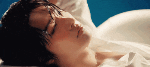 a man is laying on a bed with his eyes closed and a white shirt on