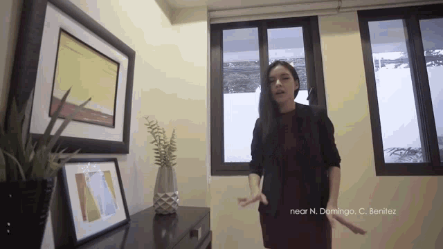 a woman stands in front of a window with near n. domingo c. benitez written on the bottom right