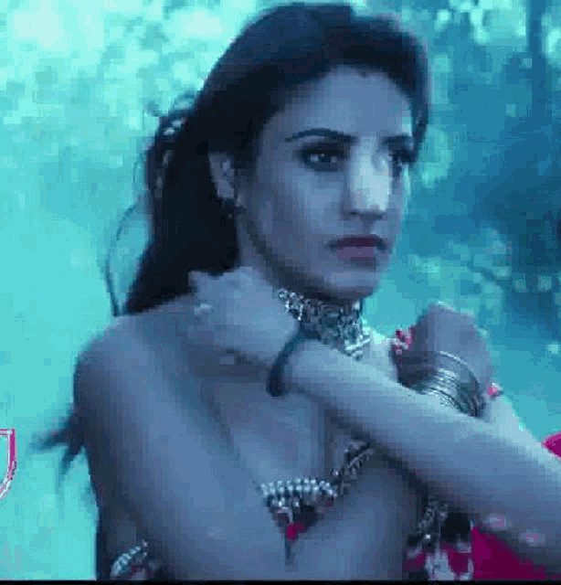 a naked woman wearing a choker and bracelets is standing in a dark room .