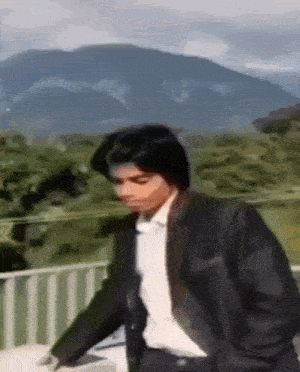 a man in a suit and tie is standing in front of a mountain .