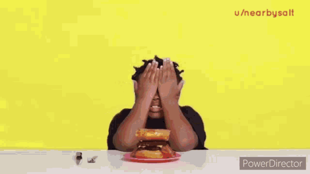 a young boy is sitting at a table with a hamburger on top of a doughnut .