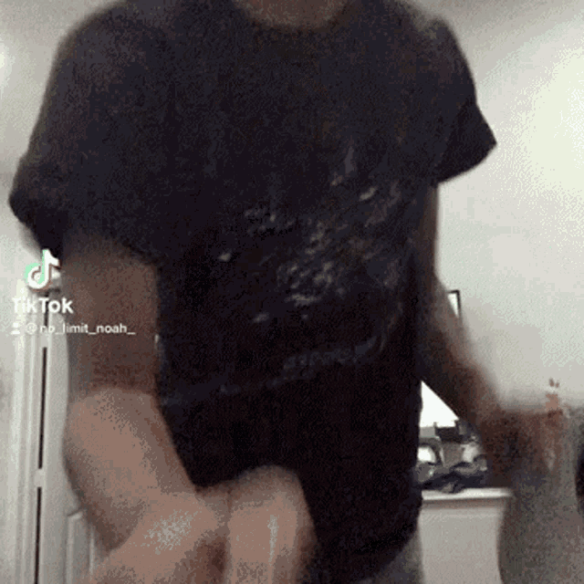 a man in a black t-shirt is dancing in a room with a tiktok video .
