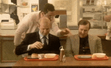 two men are sitting at a table in a fast food restaurant eating hamburgers .