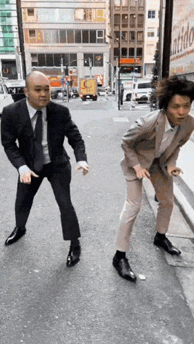 two men in suits are dancing on a street in front of buildings