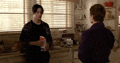 two men are standing in a kitchen talking and one is holding a carton of milk