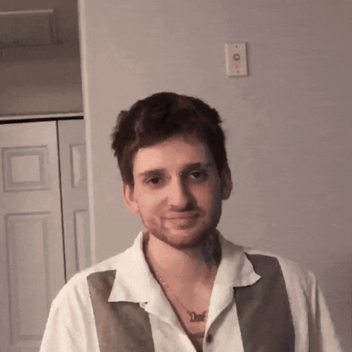 a man wearing a white shirt and a brown vest has a necklace around his neck that says devil