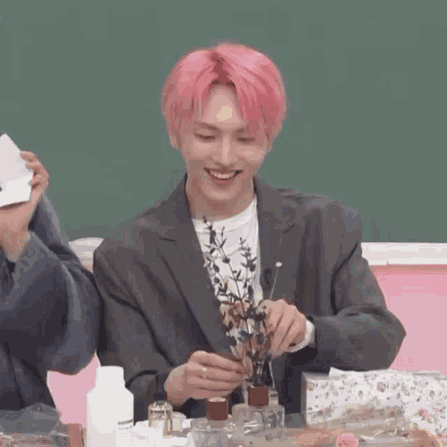 a man with pink hair is smiling while holding a vase of flowers