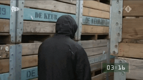 a man in a black jacket stands in front of wooden crates that say de keur on them