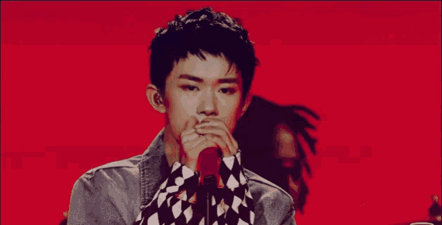 a young man singing into a microphone with a checkered shirt
