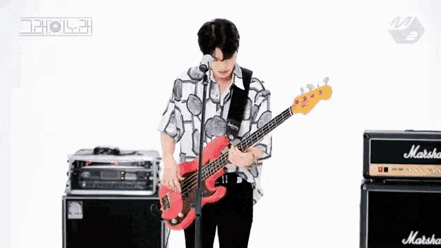 a man is playing a red bass guitar in front of a marshall amp