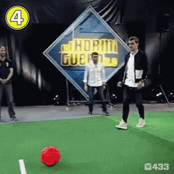 a man is kicking a red soccer ball on a field in front of a sign that says hormi guerra