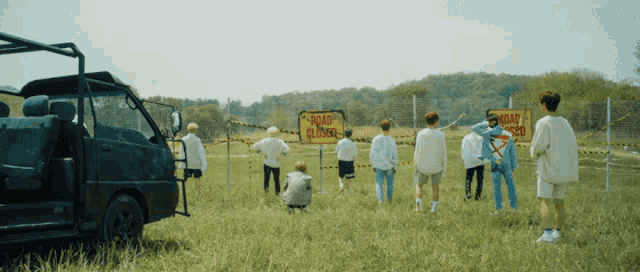 a group of people are standing in a field with a road closed sign in the background