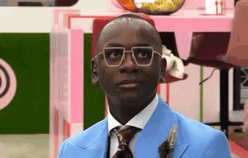 a man in a blue suit and tie with glasses is looking at the camera .