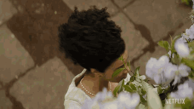 a woman in a white dress is smelling purple flowers in a netflix ad