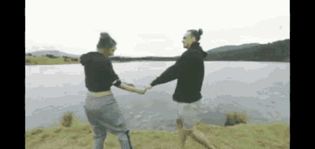 a man and a woman are holding hands while dancing in front of a lake .