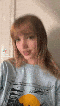 a girl with long hair is wearing a blue sweater and sticking her tongue out .