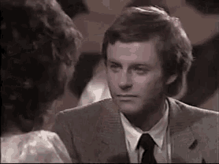 a man in a suit and tie is talking to a woman in a white dress .