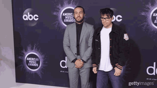 two men are standing on a purple carpet that says american music awards on it