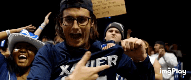 a man wearing a xavier shirt holds a sign