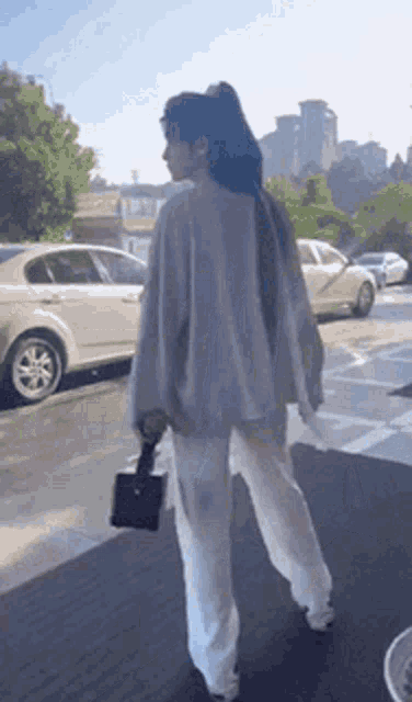 a woman wearing white pants and a grey sweater is walking down a sidewalk .