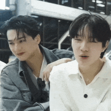 two young men are sitting next to each other with their eyes closed . one of the men is wearing a white shirt .