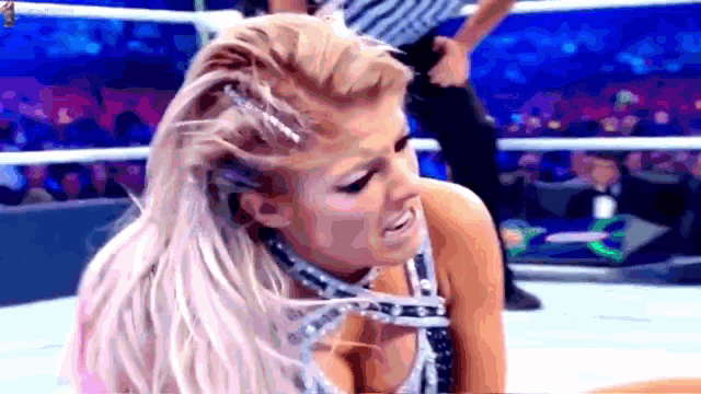 a woman is kneeling down in a wrestling ring while a referee holds her .