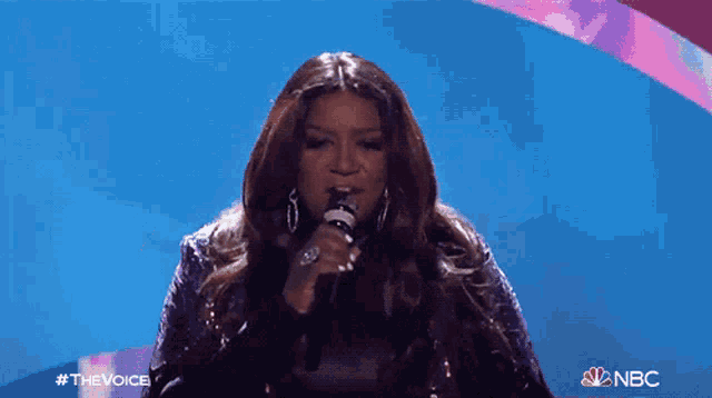 a woman singing into a microphone with nbc written on the bottom