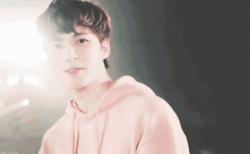 a young man wearing a pink hoodie is looking at the camera and smiling .