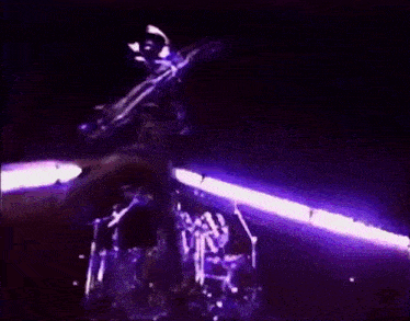 a man is playing a guitar on a stage with purple lights behind him .