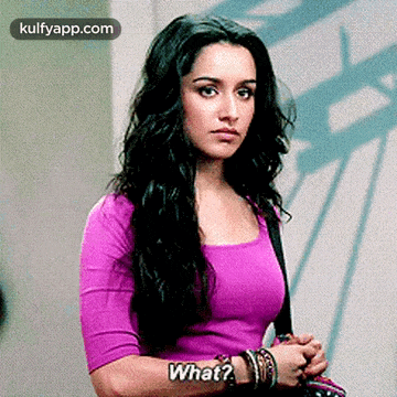 a woman in a purple shirt is standing in front of a wall and asking what ?