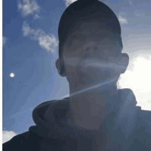 a man wearing a hat and ear buds is taking a selfie with the sun shining through his ear .