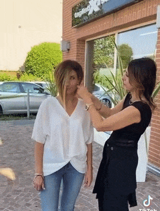 a woman in a white shirt is getting her hair cut by another woman .