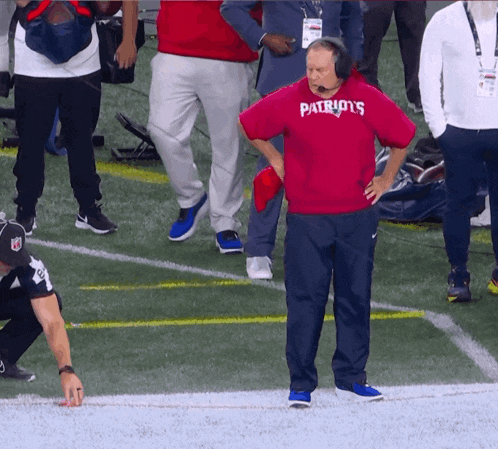 a man wearing a red patriots shirt stands on the field