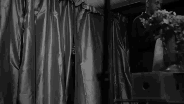 a man in a white shirt is standing behind a curtain in a black and white photo .