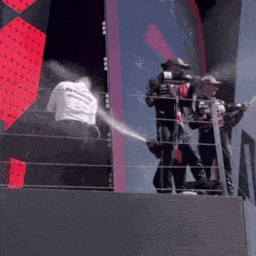 a man in a petronas shirt is spraying champagne on a podium .