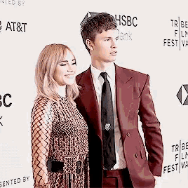 a man in a suit and tie stands next to a woman in a dress on a red carpet .