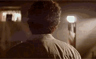 a man with curly hair is standing in a dark room looking at a light .