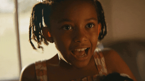 a little girl with dreadlocks is smiling with her mouth wide open