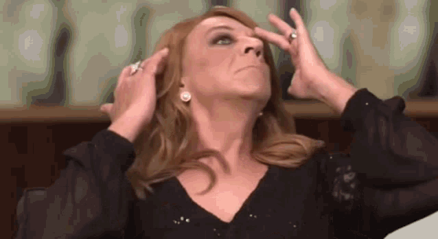 a woman is touching her face with her hands while wearing a black shirt and earrings .
