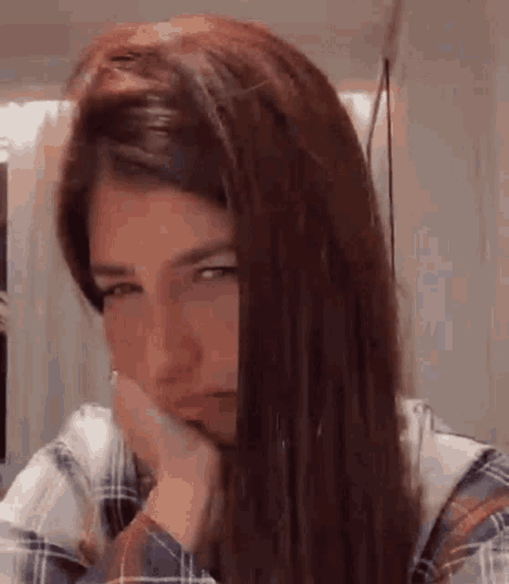 a woman with long red hair is making a funny face with her hand on her chin .
