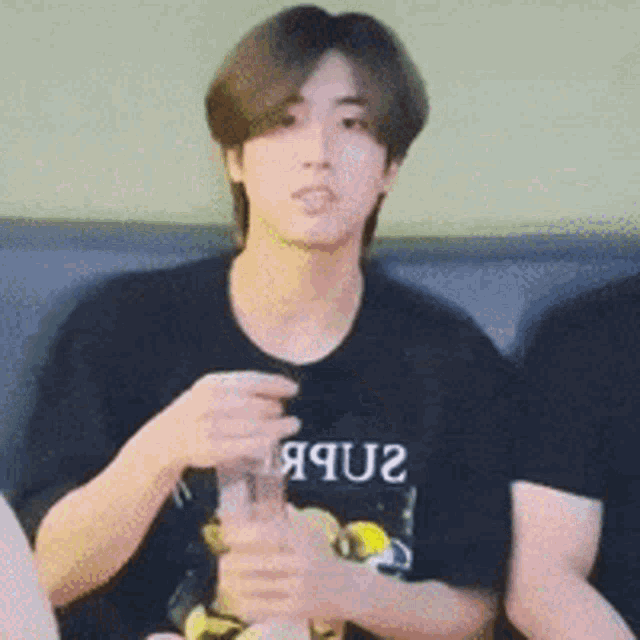 a man wearing a black t-shirt that says ' яqu2 ' on it is sitting on a couch