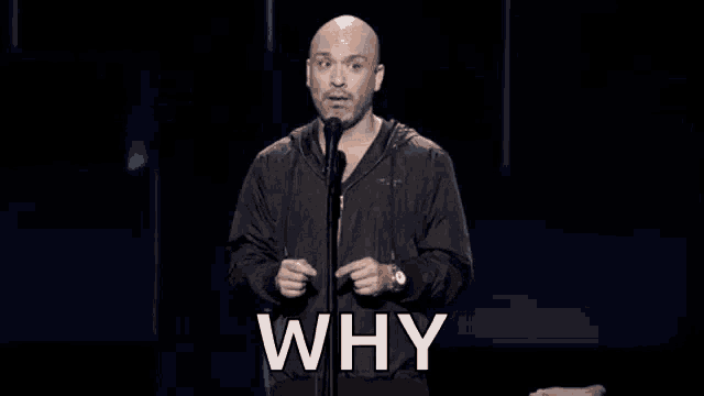 a bald man in a black jacket is standing in front of a microphone and asking why .