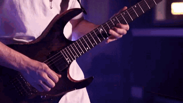 a man in a white shirt is playing an electric guitar with the letter k on the neck