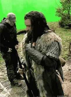 a man in a fur coat is standing in front of a green screen while holding a sword