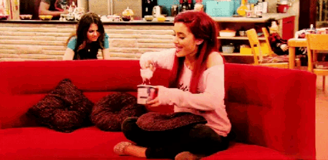 a woman is sitting on a red couch holding a cup of coffee