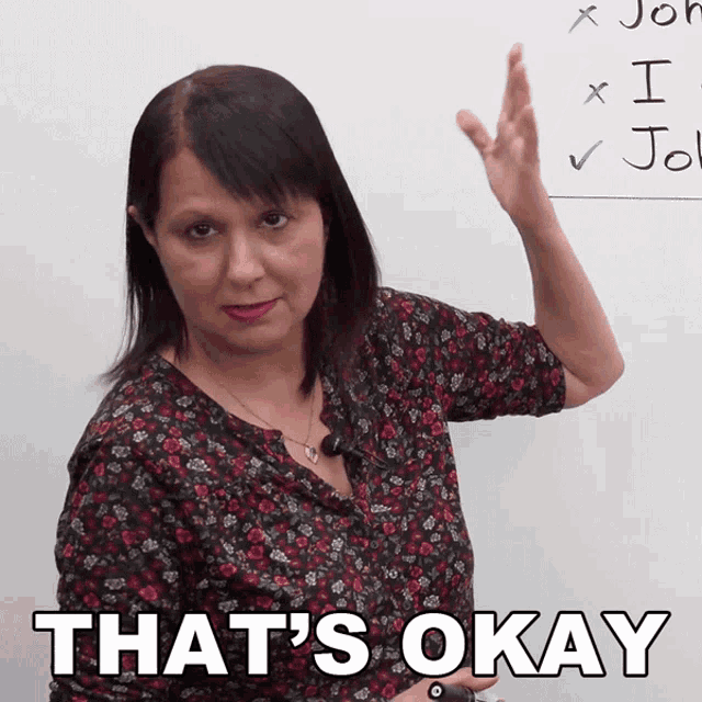 a woman in a floral shirt says that 's okay in front of a white board
