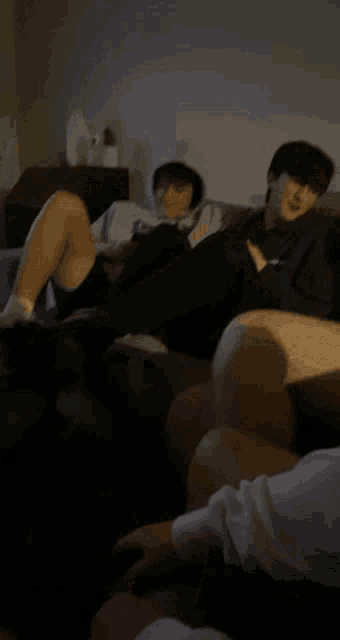 a man in a hoodie sits on a couch while another man looks at his phone