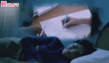 a person is writing on a piece of paper while a woman is sleeping in bed .