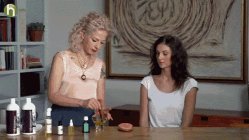 two women are sitting at a table with bottles of essential oils and a green h on the bottom