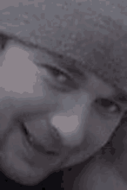 a close up of a person 's face wearing a hat and smiling in a black and white photo .